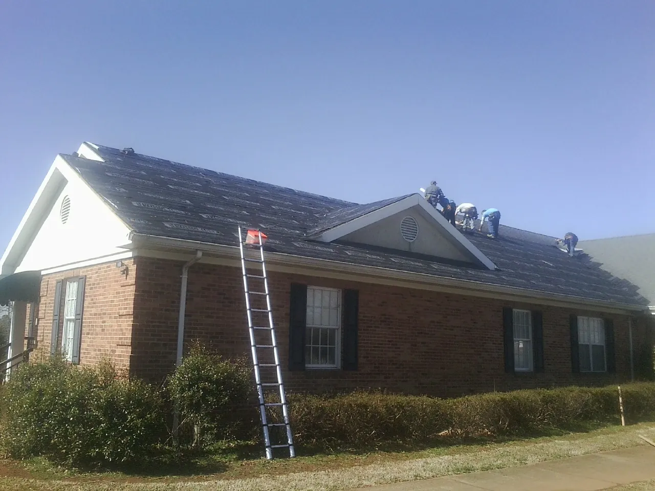 Crew tearing shingles off a brick ranch roof with a ladder set — Metal Roof Repair work by our crew in Wilbur