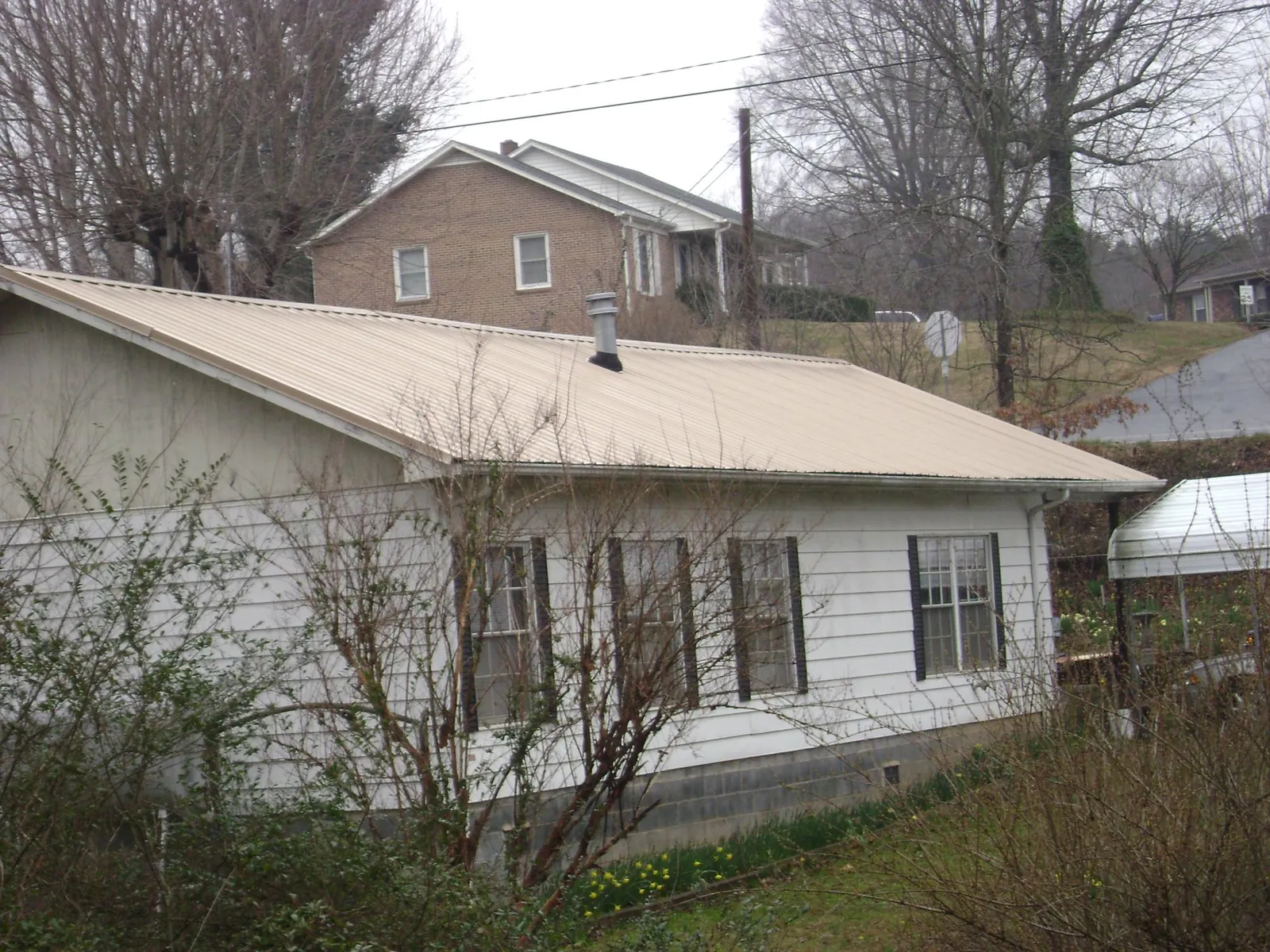Tan metal roof on a white sided house set into a hillside — Commercial Roofing by Roofing Brothers in Wilbur